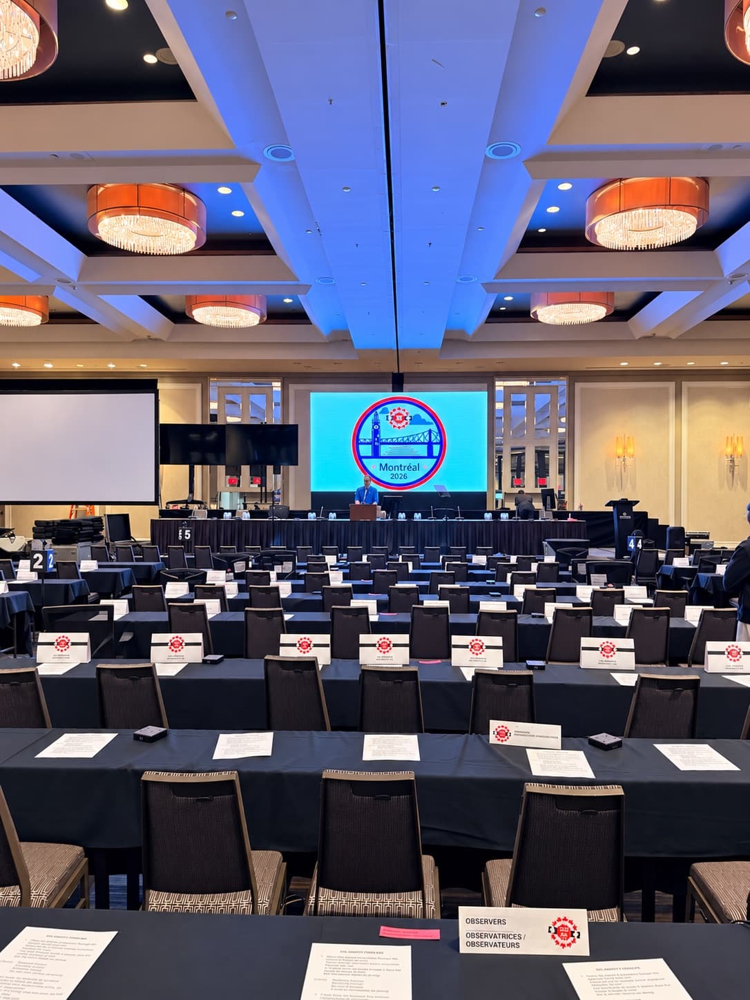 Hotel ballroom set for a conference with delegate tables facing an LED display at the head table